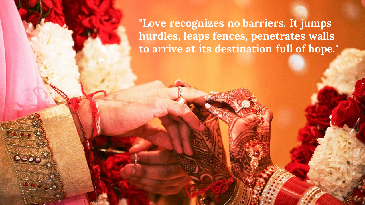 Close up of two hands exchanging wedding rings, with traditional Indian attire and red floral decorations.