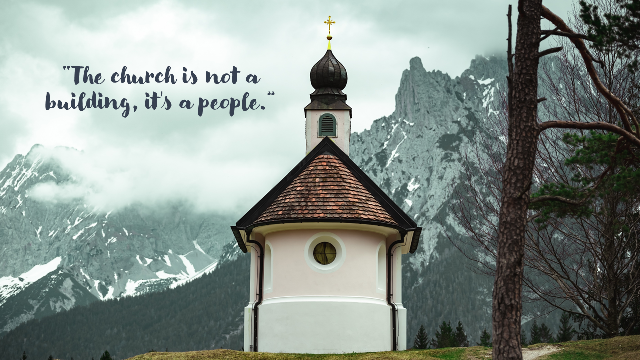 Chapel with a distinctive round shape and a peaked roof, set against a backdrop of snow capped mountains and cloudy skies.